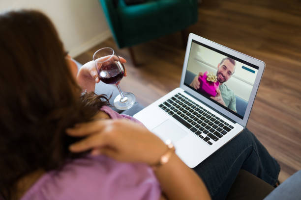 Rear view of a long distance relationship couple having a romantic video call with wine and flowers using online technology. Credit: Antonio_Diaz. 