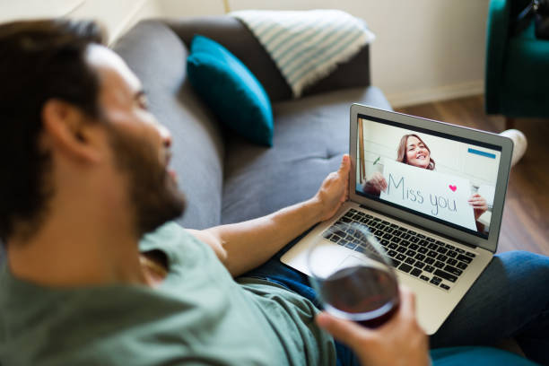 A man seen from behind drinking wine while talking to his long-distance girlfriend using technology for a video call. Credit: Antonio_Diaz. 